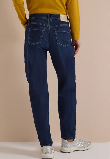 Rückansicht einer Person in blauen Jeans, gelbem Pullover und grauen Sneakern.
