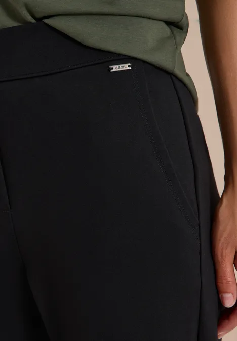 Pantalon noir souple avec poches latérales et petit label métallique discret à la taille.