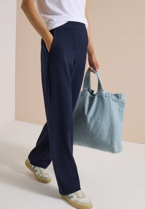 Personne portant un pantalon bleu marine ample, des baskets blanches et un sac en denim bleu clair.