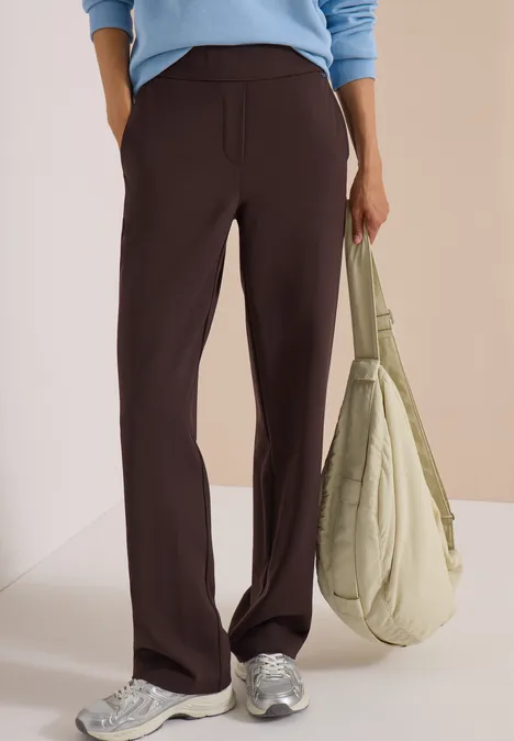 Personne porte un pantalon fluide marron foncé, un haut bleu clair, des baskets blanches et un sac vert pâle.