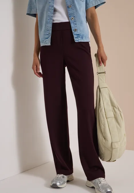 Femme en pantalon ample prune, veste jean courte bleue, baskets argentées et grand sac beige.