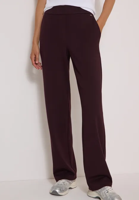 Femme porte un pantalon aubergine droit avec poches et baskets blanches.