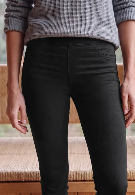 Une personne porte un pantalon noir moulant et un pull gris, cadrés de la taille aux genoux.