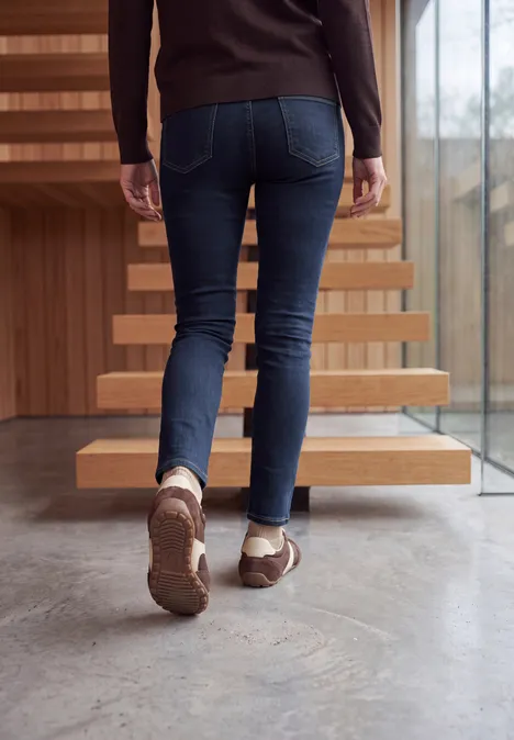 Eine Person in Jeans und braunen Schuhen steigt eine moderne Treppe hinauf.