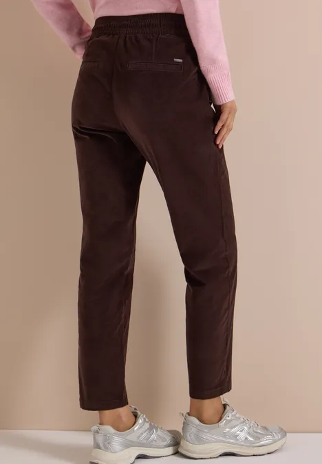 Mid Waist Slim Leg Hose im Casual Fit truffle brown Frau trägt braune Cordhose und silberne Sneaker, Blick von hinten, kombiniert mit rosa Oberteil.