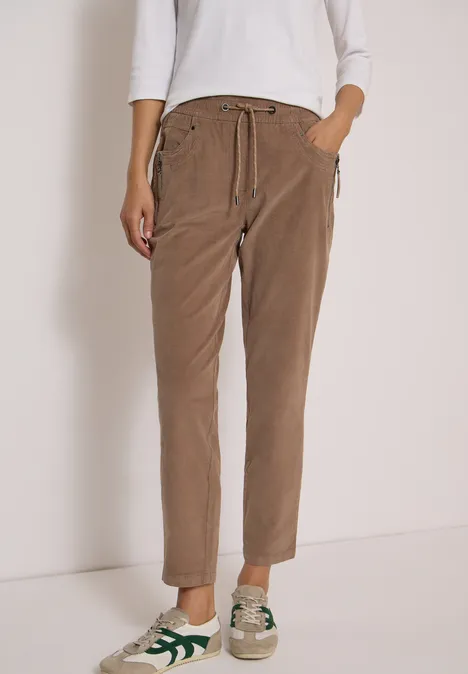 Mid Waist Slim Leg Hose im Casual Fit earthy taupe Beine in lockeren beige Cord-Hosen mit Kordelzug und lässigen Sneakers vor weißem Hintergrund.