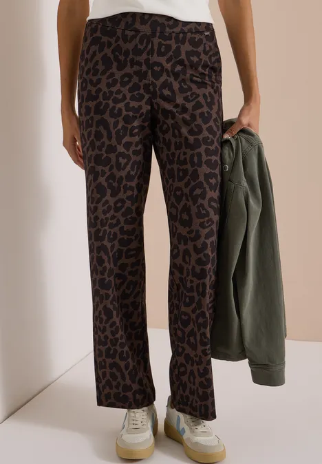 Frau trägt gerade geschnittene Leoprint-Hose und hält eine olivgrüne Jacke.