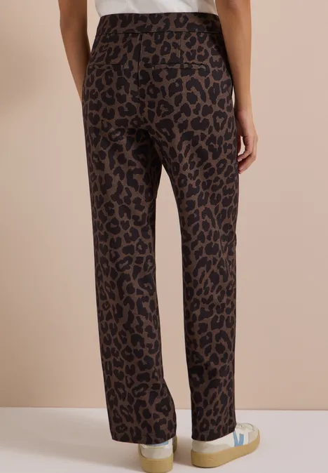 Person von hinten: braune, gerade geschnittene Hose mit Leopardenmuster und weißen Sneakern.