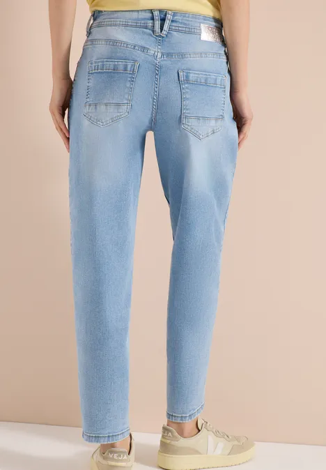 Achteraanzicht: persoon draagt lichtblauwe jeans met relaxte pasvorm, taps toelopende pijpen en beige sneakers.