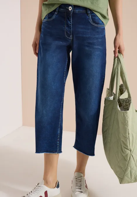 Damen-Cropped-Jeans in dunklem Denim mit weißen Sneakern und grünem, gesteppter Shopper.