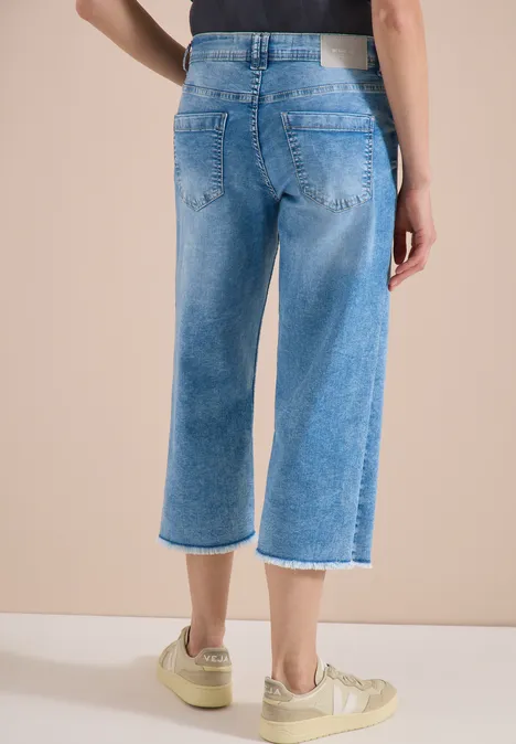 Achteraanzicht van een persoon in lichtblauwe, wijde cropped jeans met rafelige zoom en beige sneakers