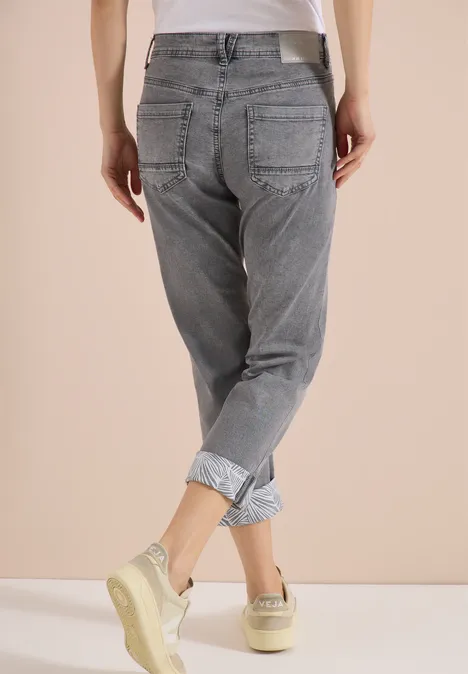 Rugaanzicht van een persoon in grijze omgezoomde spijkerbroek en sneakers voor een neutrale achtergrond