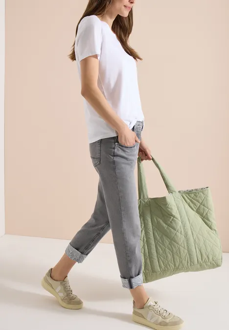 Vrouw in wit T-shirt, grijze opgerolde jeans en groene sneakers draagt grote gestikte groene tas.