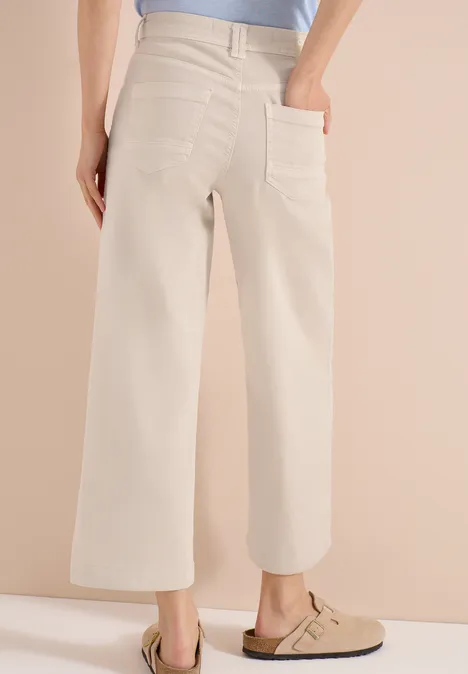 Pantalon large beige taille haute avec poches plaquées, porté avec des sabots beiges.