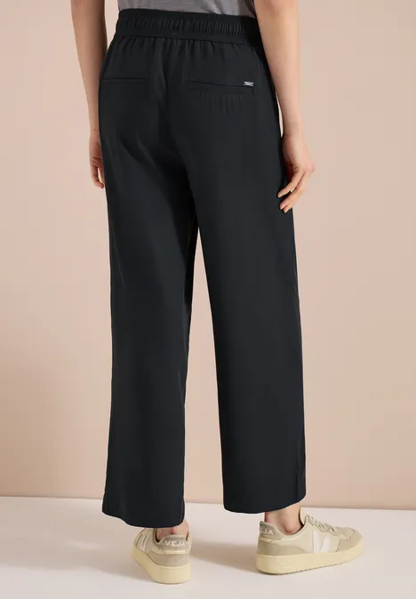 Rückansicht einer Person in locker sitzender, weiter schwarzer Hose mit elastischem Bund und Seitentaschen.