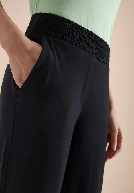 Nahaufnahme einer schwarzen Hose mit elastischem Bund und Taschen, Hand in Tasche, grünem Oberteil.