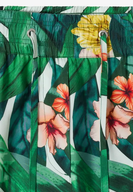 Grüne Badeshorts mit tropischen Blättern und bunten Hibiskusblüten in Orange und Gelb.
