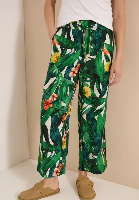 Weite Hose mit grünem Dschungelprint und Blumen, kombiniert mit beigen Slippern.