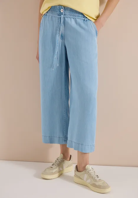 Losvallende lichtblauwe wijde jeans met koordsluiting tot de enkels, gecombineerd met beige sneakers.