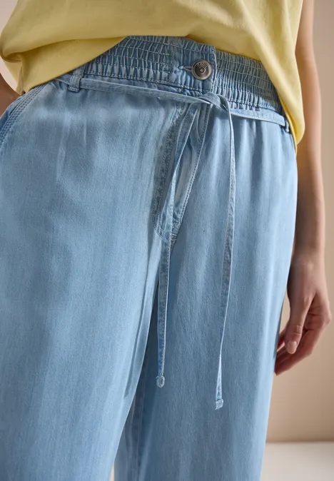 Lichtblauwe, losse broek met elastische taille en trekkoord, gedragen door een persoon.