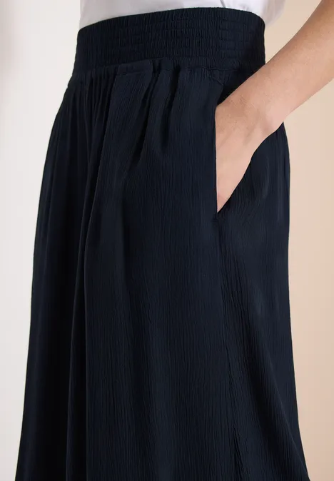 Dunkelblaue, weite Hose mit elastischem Bund und seitlichen Taschen, feine Textur und Falten.