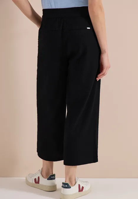 Zwart, wijd broek met elastische taille en zijzak, op enkels, gecombineerd met lichte sneakers met rood-blauwe accenten.