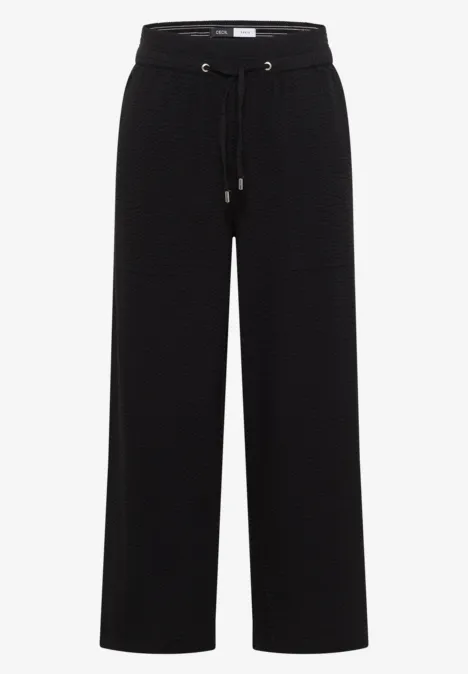 Zwarte, wijde broek van stof met hoge taille en trekkoord.