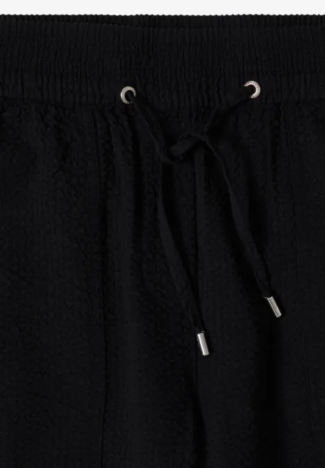 Zwart, gewafeld textiel met elastische tailleband en aantrekkoord met metalen uiteinden.