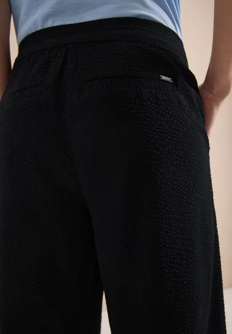 Zwarte, gestructureerde broek met elastische taille en achterzak van dicht geweven stof.