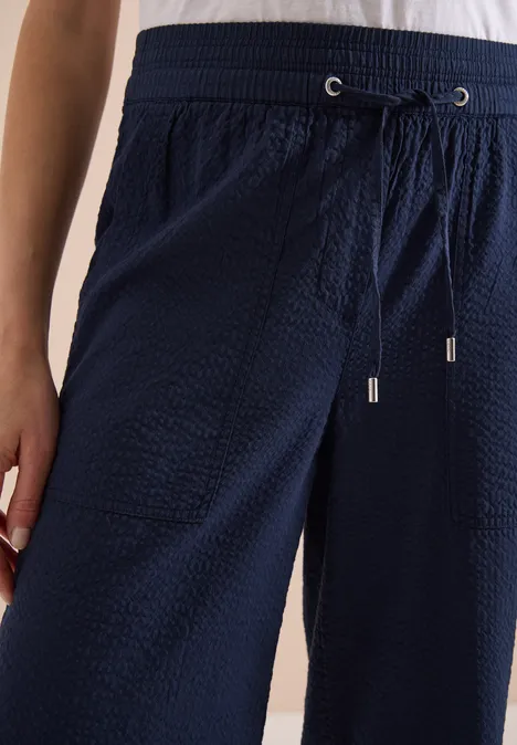 Close-up van een donkerblauwe, gestructureerde broek met elastische taille en aantrekkoordje.