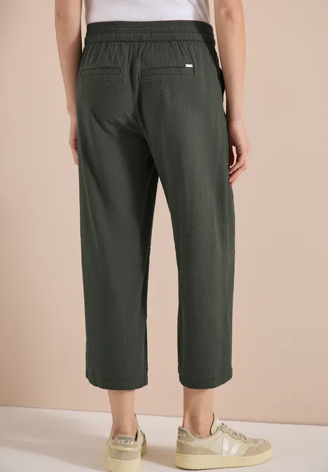 Moderne, dunkelgrüne 3/4-Hose, weit geschnitten mit elastischem Bund und Tasche, dazu beigen Sneaker.