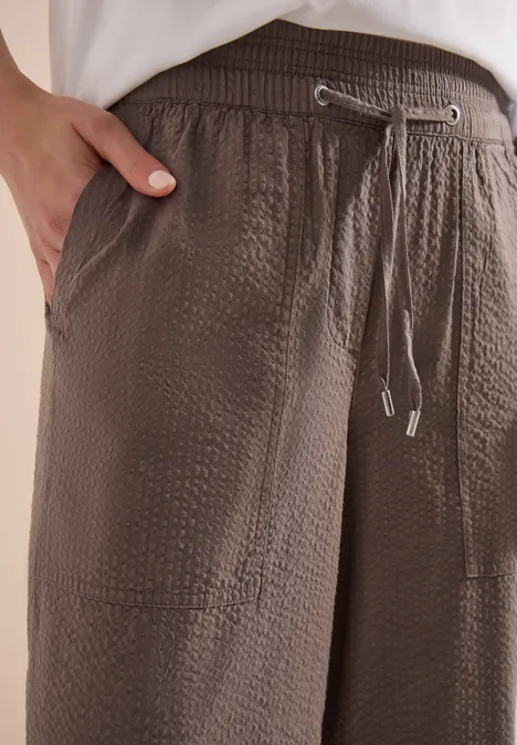 Nahaufnahme einer braunen, strukturierten Hose mit elastischem Bund, Tunnelzug und seitlicher Tasche.