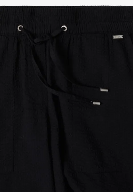 Schwarze Hose mit Waffelstruktur, elastischem Bund und Kordelzug mit silbernen Endstücken.