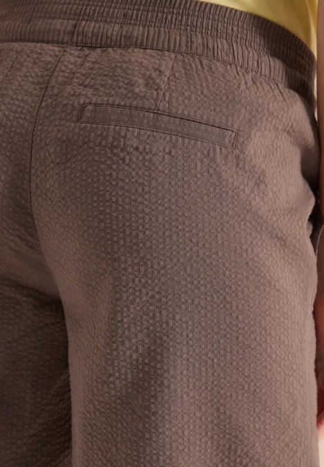 Nahaufnahme einer braunen, strukturierten Hose mit Gesäßstasche und goldenem Taillenbund.