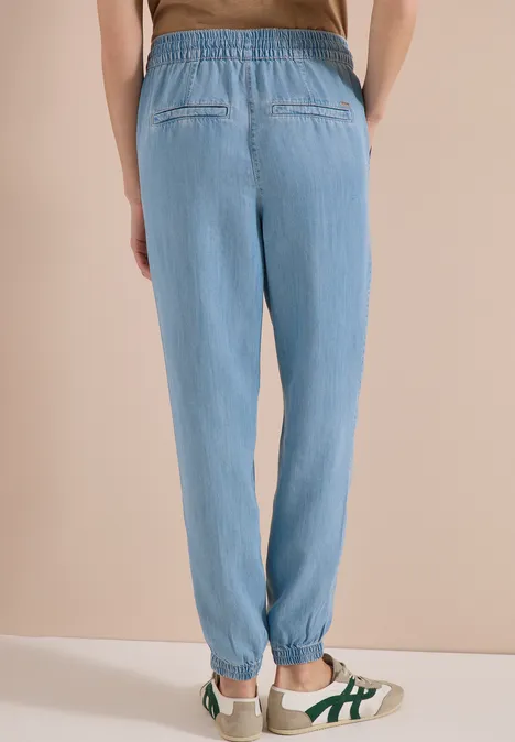 Achteraanzicht van een persoon in losse lichtblauwe joggingsbroek met elastische taille en witte sneakers.