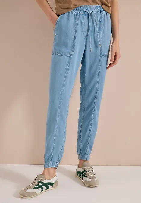 Lichtblauwe joggingbroek met trekkoord en witte sneakers met groene accenten.