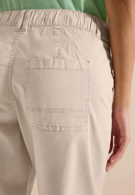 Detailaufnahme: Person in beigen Hosen mit aufgesetzter Tasche, grünes Oberteil, Rückansicht.