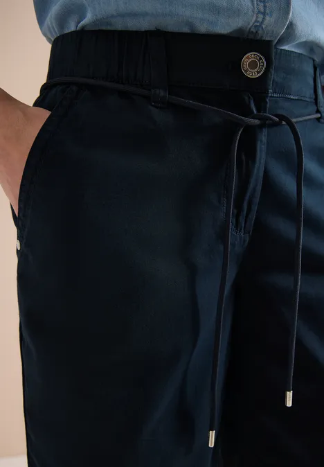 Nahaufnahme einer dunkelblauen Freizeithose mit Kordelzugbund, Knopf und seitlicher Tasche.