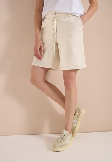 Person trägt weißes T-Shirt, kniehohe beige Shorts und helle Sneaker.