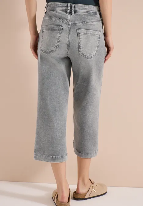 Rückenansicht einer Person in grauen, locker sitzenden, knöchellangen Jeans und beigen Sandalen.