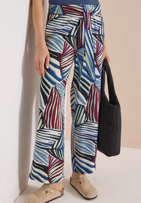 Pantalon large en tissu à motif de feuilles abstraites bleu, bordeaux et blanc, lien à la taille, accompagné d’un sac noir.