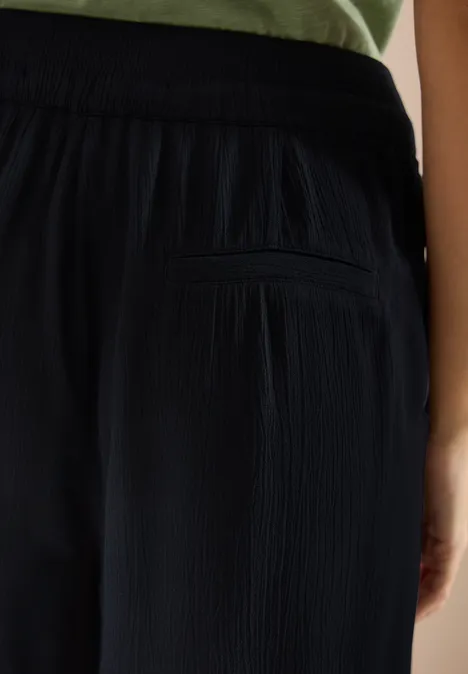 Personne vue de dos portant un pantalon noir texturé avec poche arrière zippée