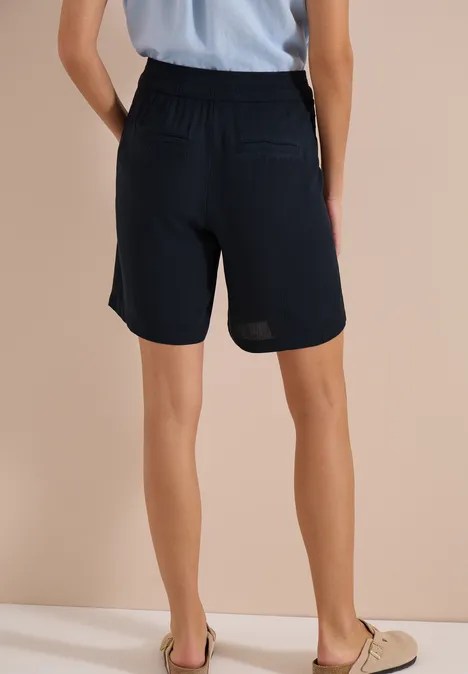 Achteraanzicht van een persoon in lichtblauw shirt en donkere kniebroek voor een beige achtergrond