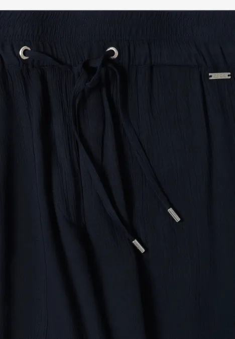 Close-up van een zwarte, gestructureerde broek met elastische taille en koord met zilverkleurige uiteinden.