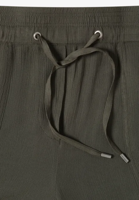 Close-up van een olijfgroene broekband van stof met elastische taille en trekkoord.
