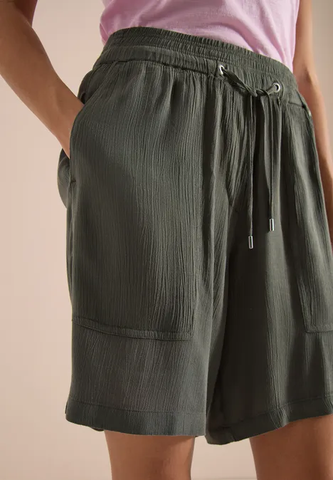 Olijfgroene korte broek met trekkoord, opgestikte zakken en fijne ribstructuur, losvallend tot net boven de knie.