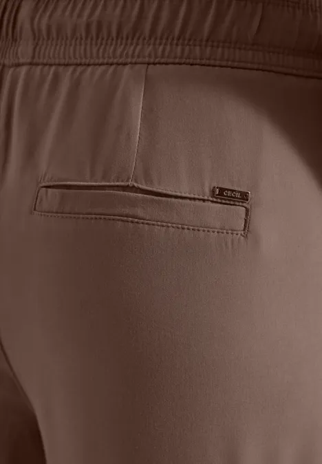 Close-up van de achterkant van een bruine broek met elastische taille en geïntegreerde ritszak.
