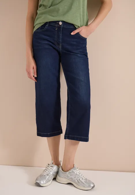 Blaue Cropped-Jeans mit weitem Bein und silbernen Sneakern an den Füßen.