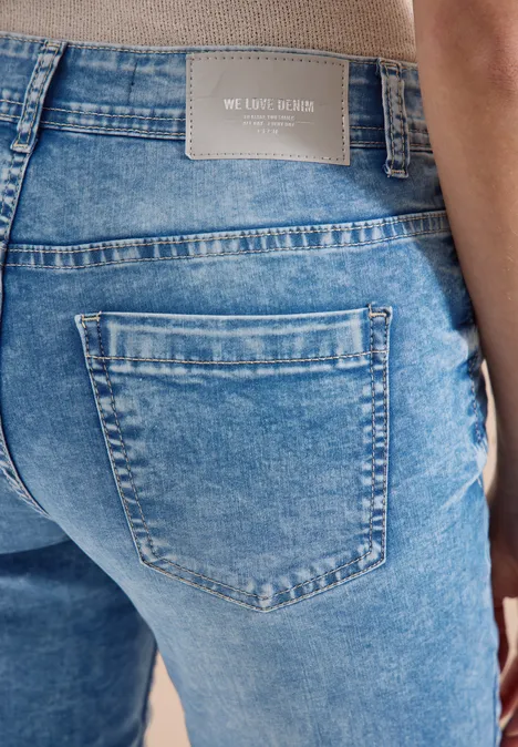 Achteraanzicht van een persoon in blauwe spijkerbroek met 'WE CARE LABEL' label op de tailleband.
