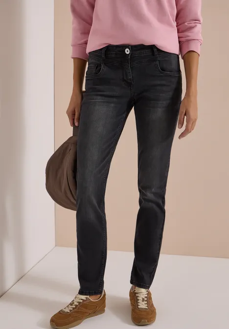 Frau mit rosa Pullover, dunklen Jeans, braunen Sneakern und Beuteltasche.